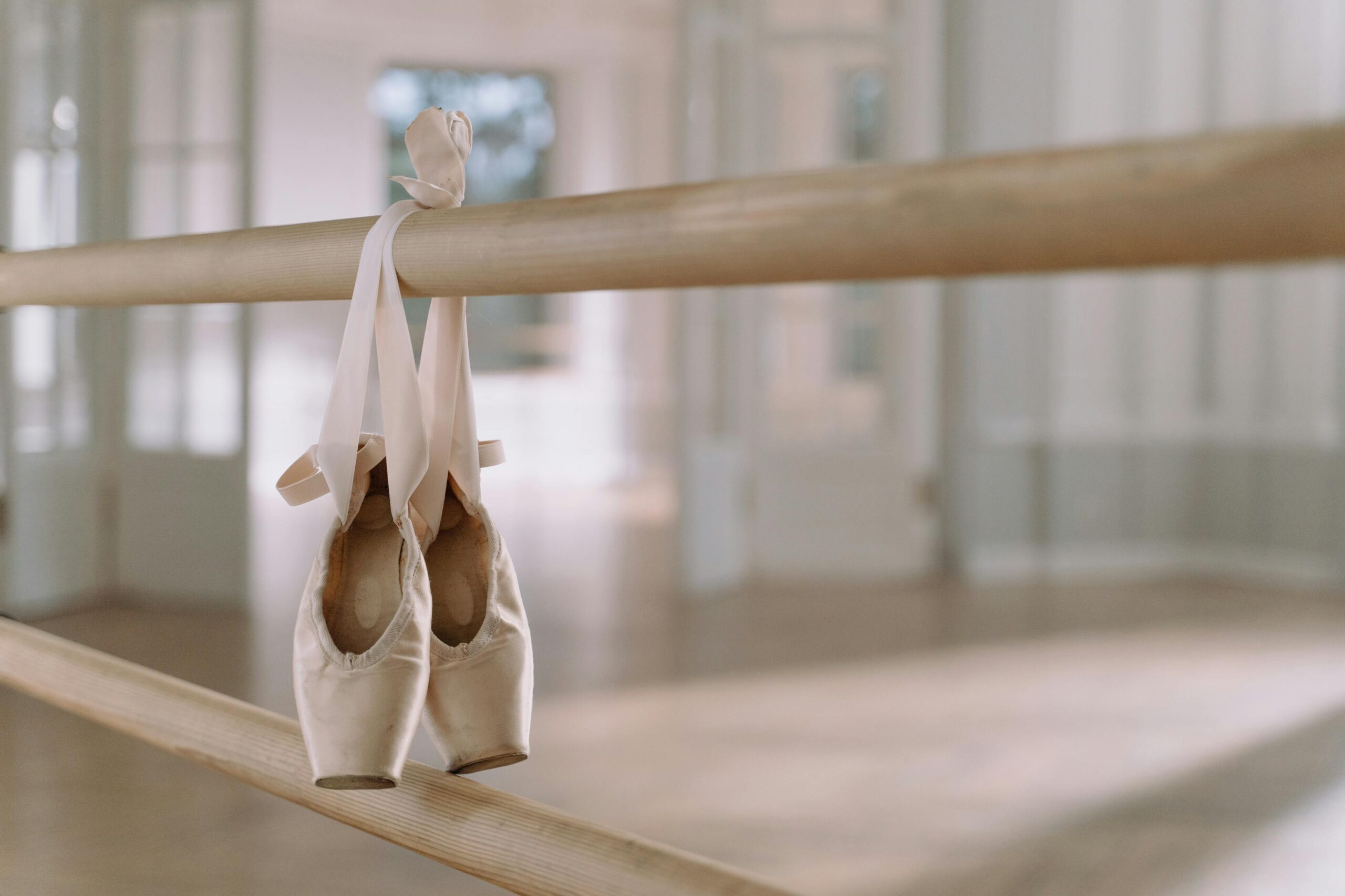 Close-up of ballet pointe shoes hanging on a barre in a dance studio.